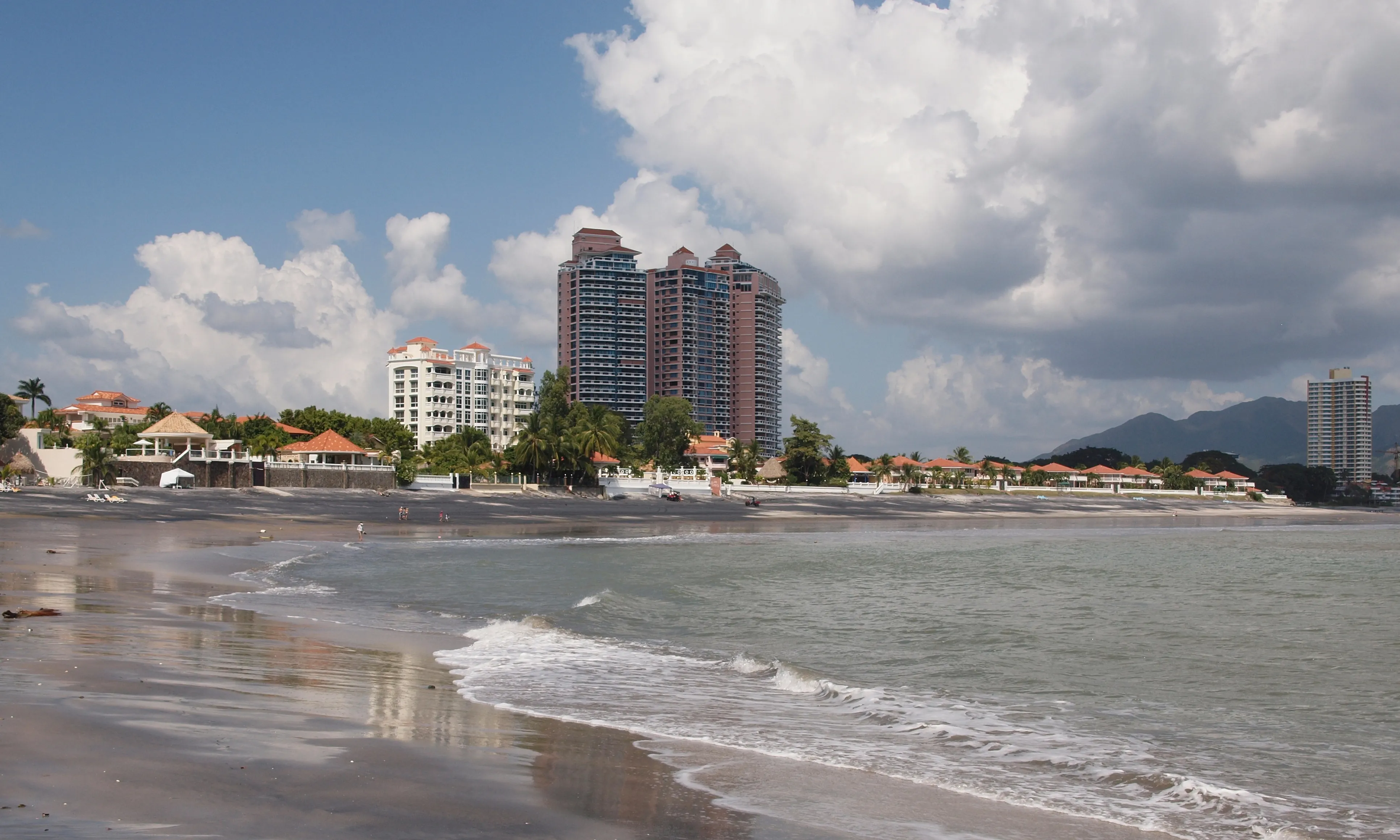 Playa Coronado with beachfront condo towers, palm trees and waves under a blue sky